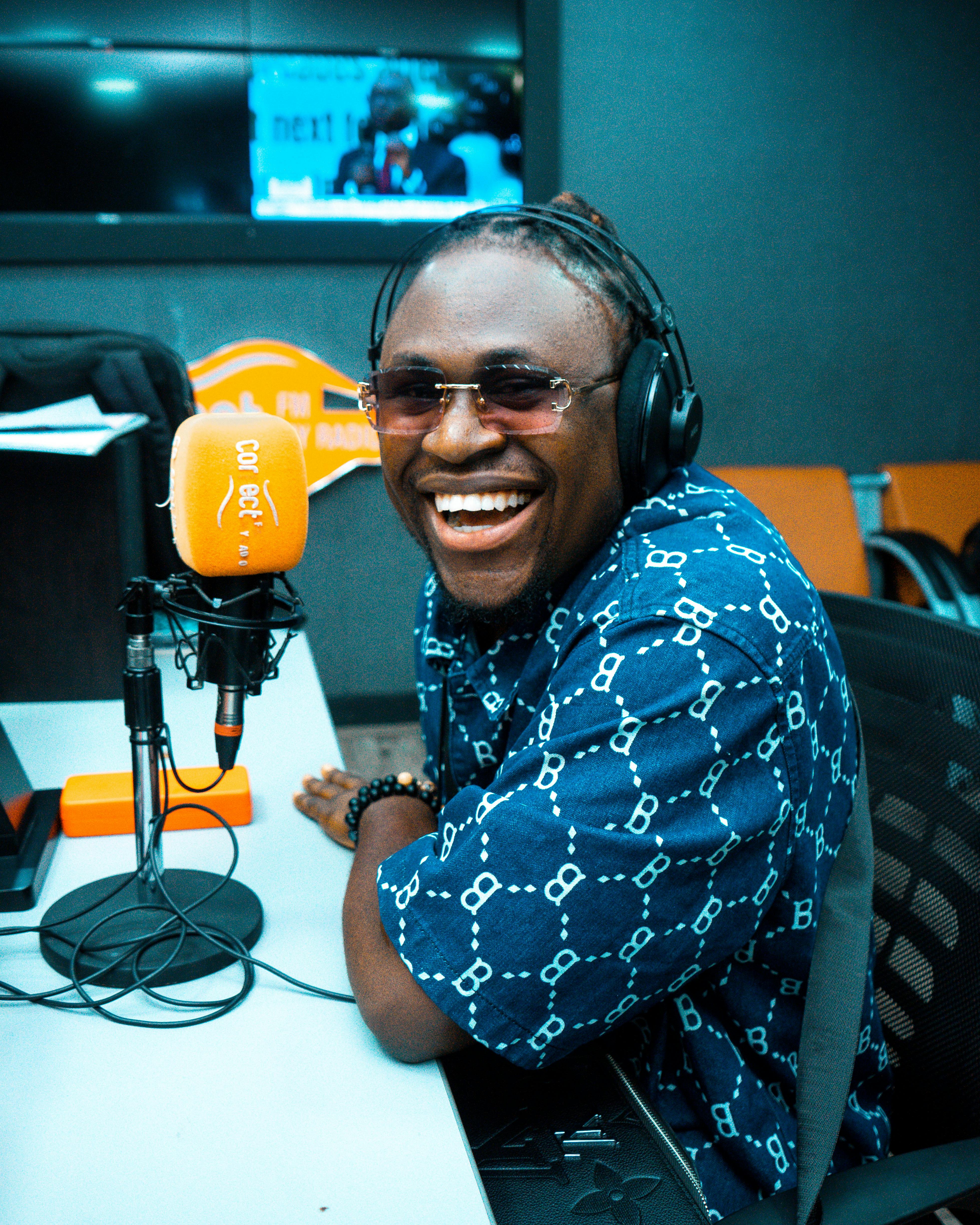 Smiling man wearing headphones speaks into a microphone at a radio studio.