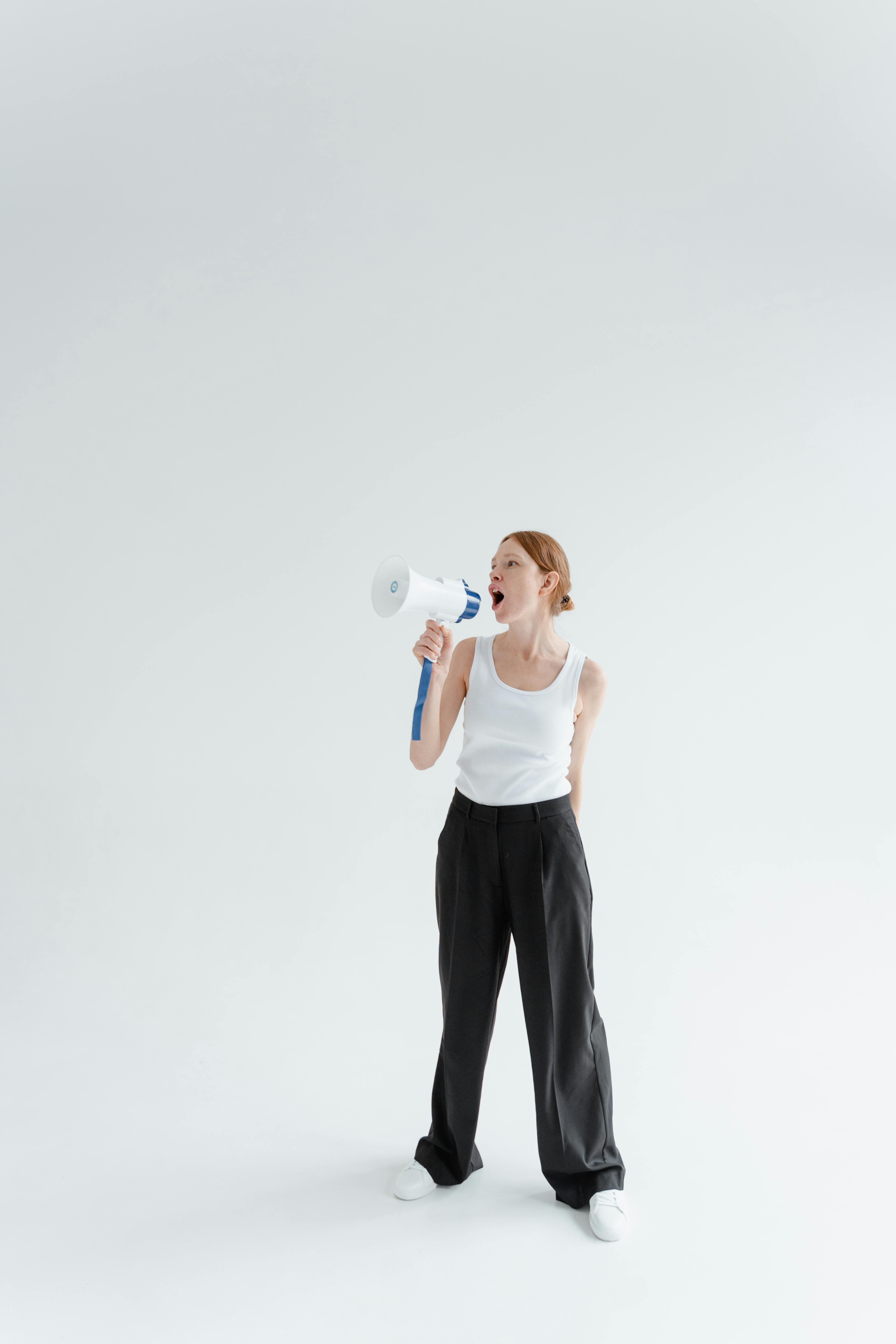 Woman shouting through a megaphone in a studio with a white background, expressing emotion.