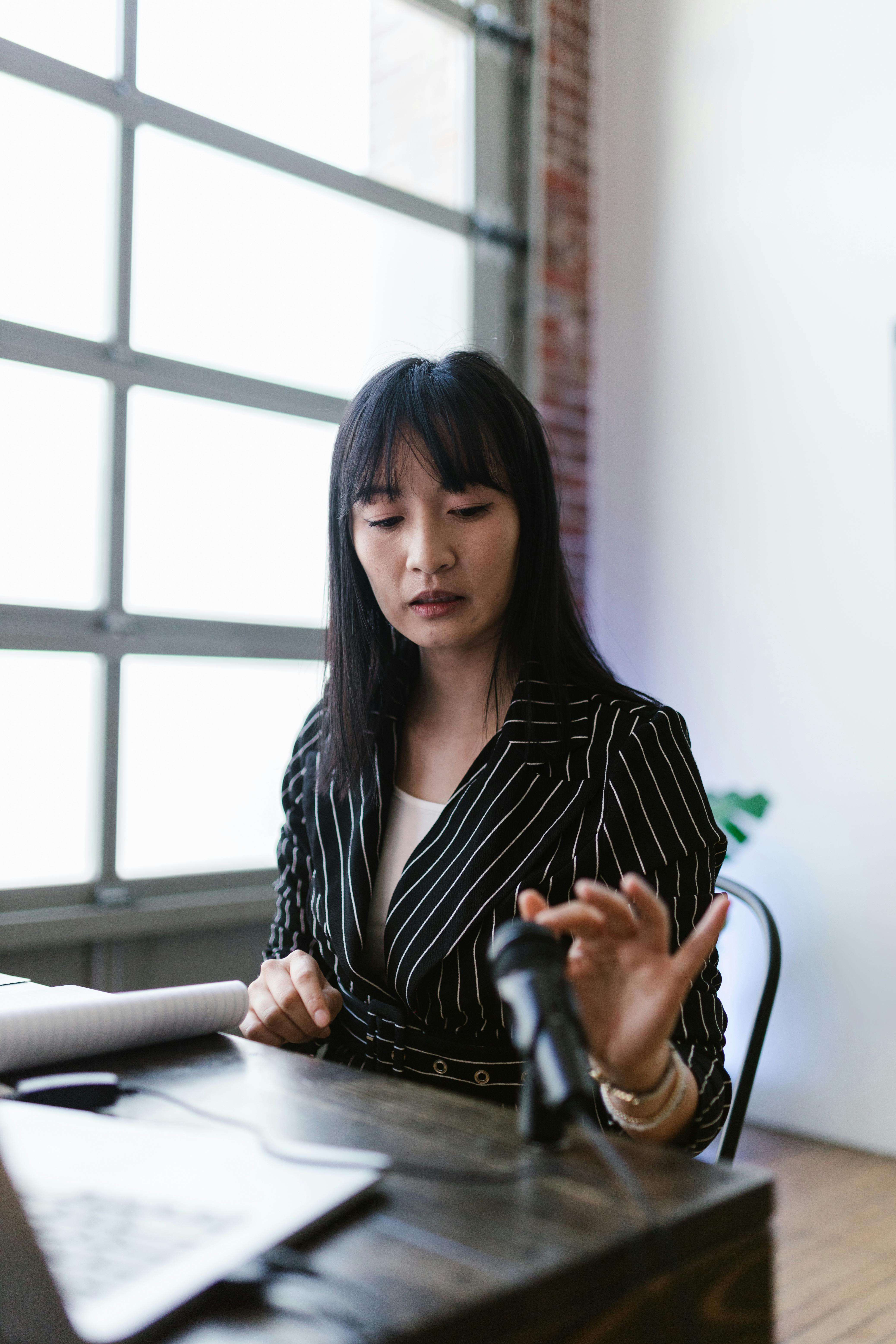 Asian woman in striped jacket speaking at a podium, indoors.